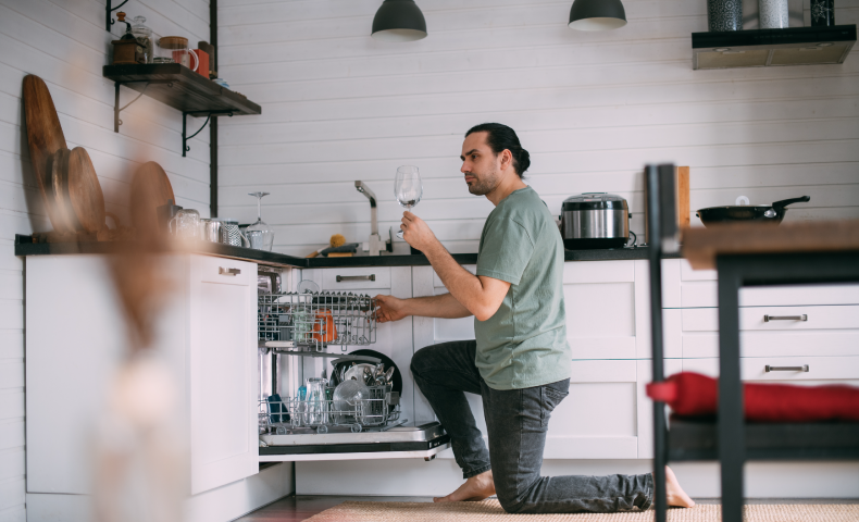 a man examines a wine goblet while loading a kitchen dishwasher