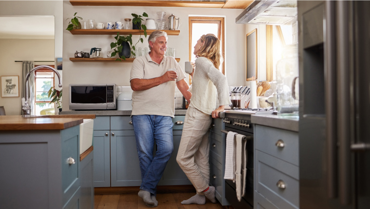 a middle aged couple smiles in a well-appointed and well-lit kitchen