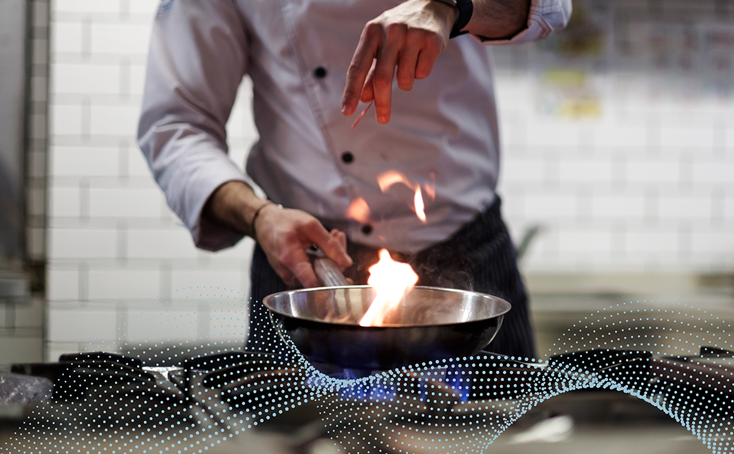 a chef drops ingredients into a stainless steel wok