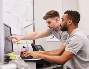 two workers review work on a large desktop screen