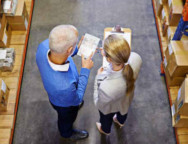 Two warehouse workers review a supply manifest